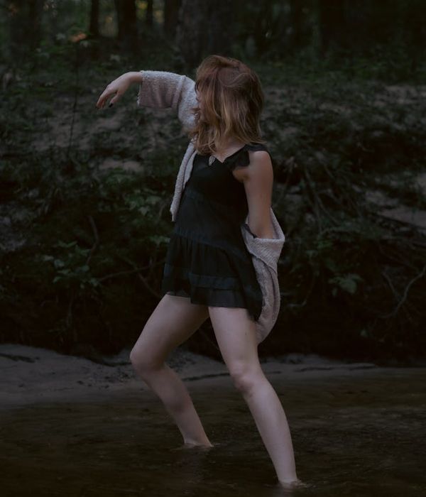 A woman in a calm, flowing movement pose against a dark background.